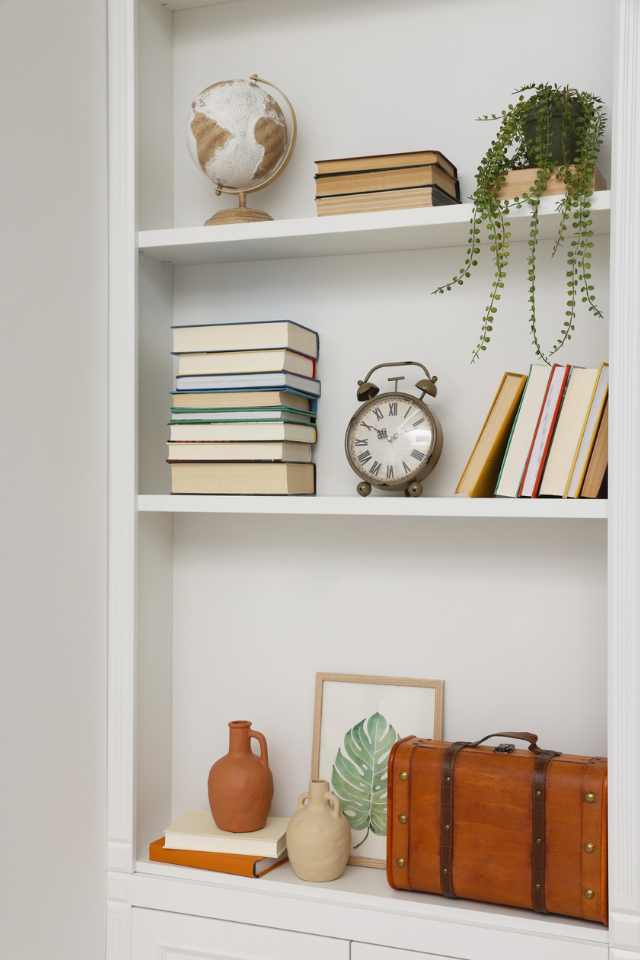 vertical white shelving in home office nook with artwork, books, and greenery